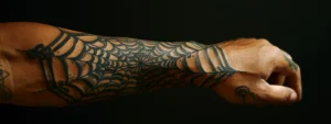 a tattooed forearm with a striking and intricate spiderweb design representing strength and resilience.